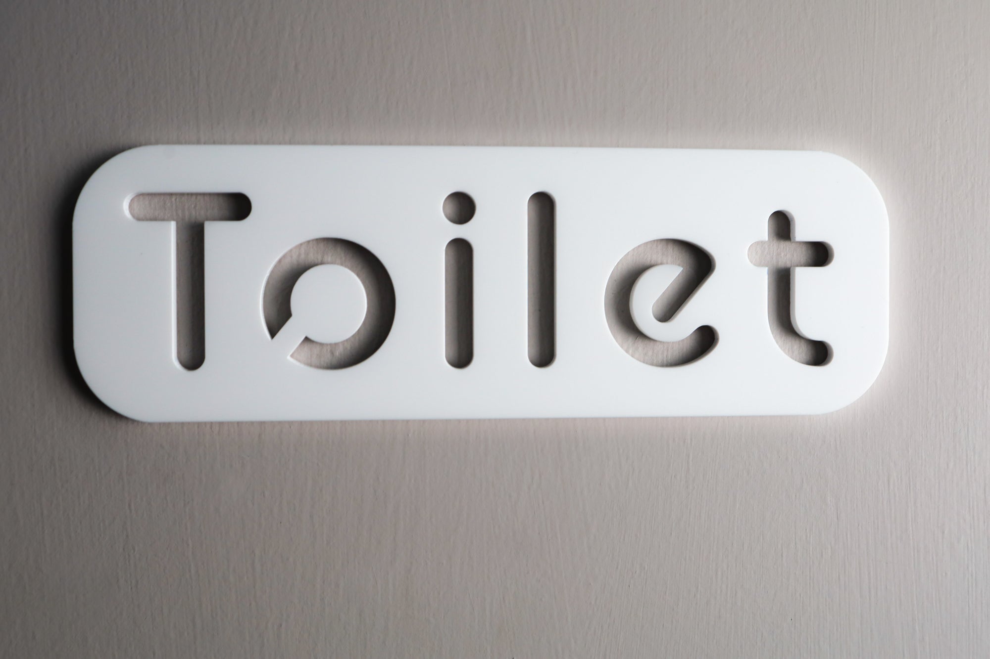 Modern white acrylic toilet sign with minimalist design and stone texture.